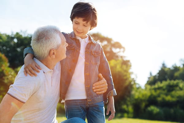 A senior man interacts with a young boy in a sunny outdoor setting
