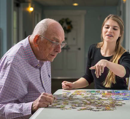 An elderly man and a staff member working on a puzzle together