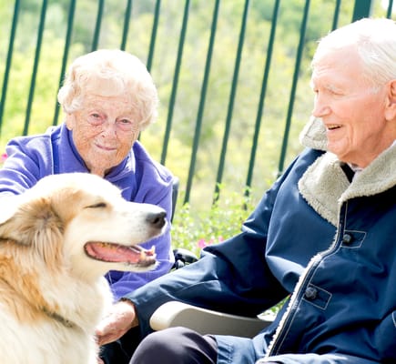 Two residents smiling outdoors with a dog