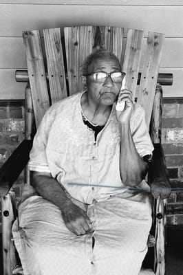 Elderly woman seated on a porch speaking on the phone