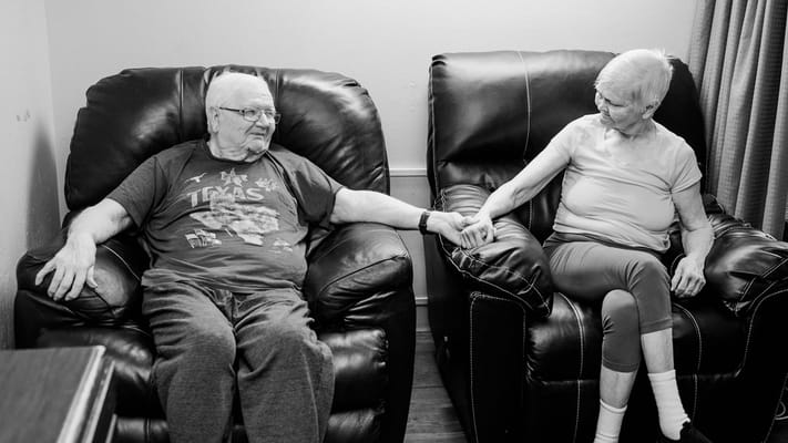 Elderly couple holding hands in comfortable chairs