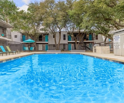 Swimming pool surrounded by trees and lounge chairs