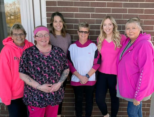 Staff posing together in pink attire outside.