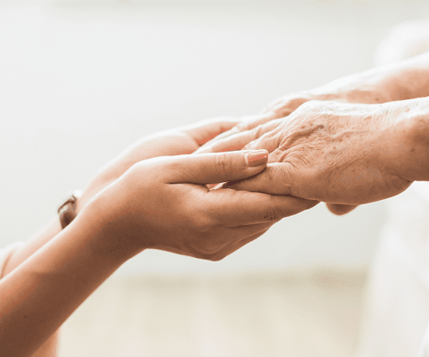 A caregiver holding an elderly person's hand