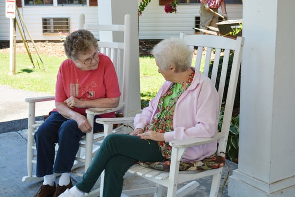 Two residents enjoying conversation on rocking chairs outside