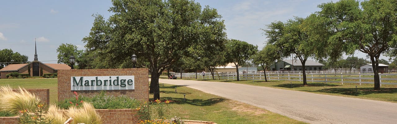 Entrance sign of Marbridge Village with trees and road