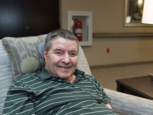 A resident smiling in a comfortable chair in the facility