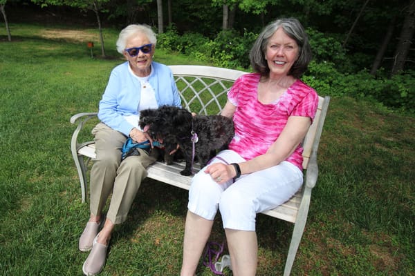 Two women sitting on a bench with a dog in the garden