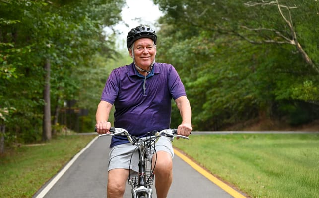 Senior man riding a bicycle on a tree-lined path