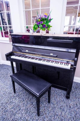 Piano in a well-lit common area with flowers