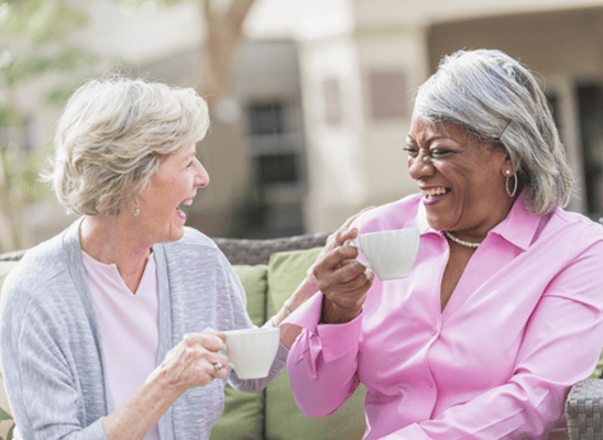 Two women enjoying tea outdoors in a sunny setting