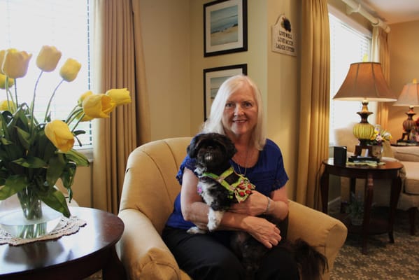 Resident sitting in a common area with a dog and flowers