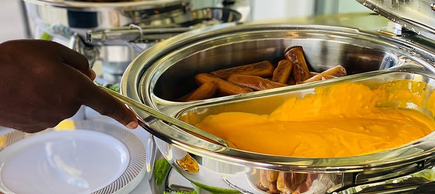 A hand serving food from a buffet tray.