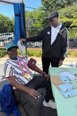 Staff member checking a resident's vitals at an outdoor health event.