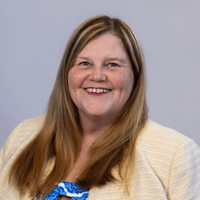 Smiling staff member with long hair and a light blazer