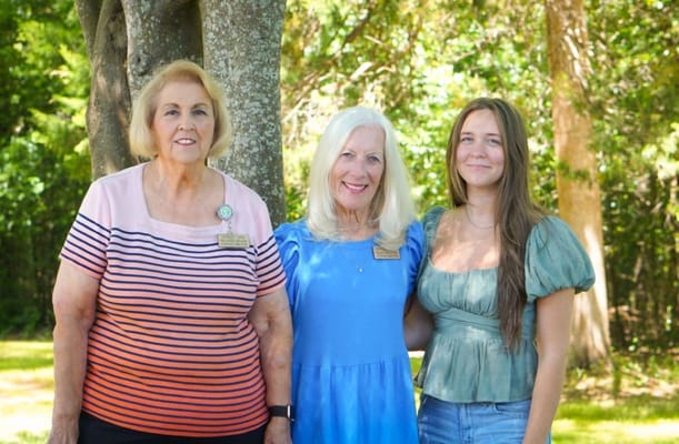 Three women smiling outdoors in a garden setting