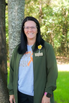 Staff member smiling outdoors near a tree