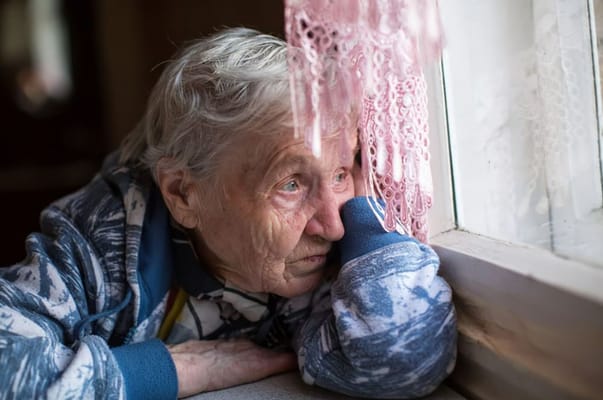 Elderly woman looking out the window in quiet contemplation.
