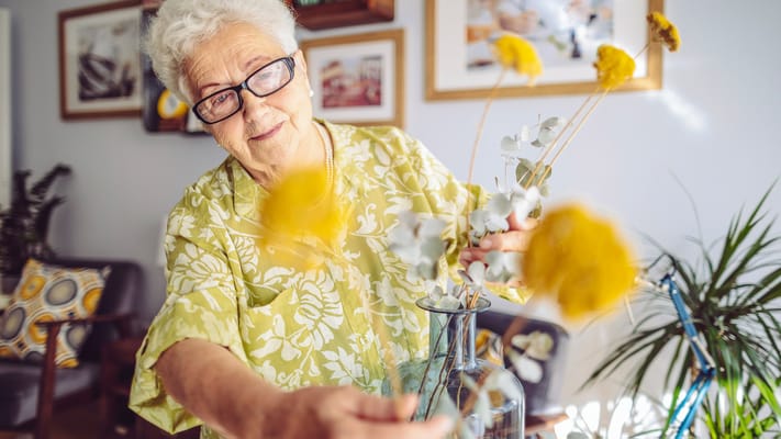 A senior woman arranging flowers in a bright room