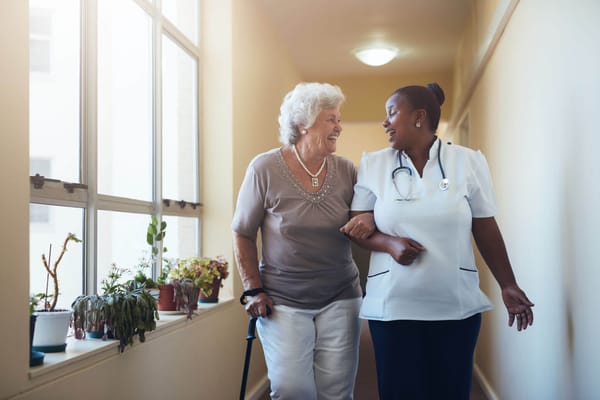 A nurse assisting a smiling resident in a corridor