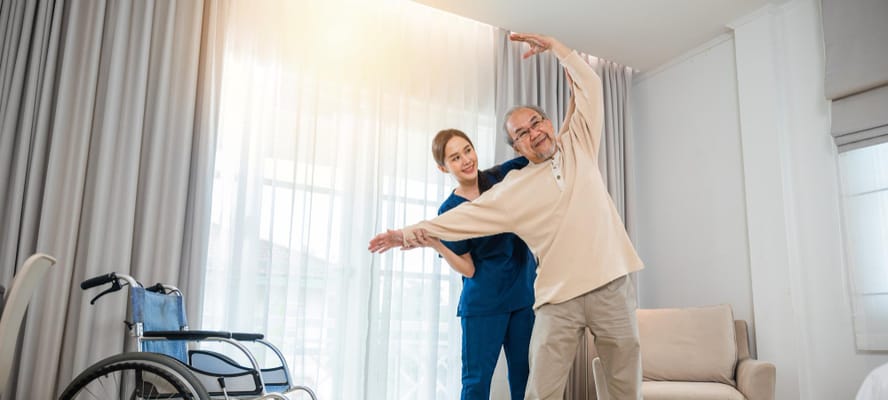 Staff assisting a resident with exercises in a bright room