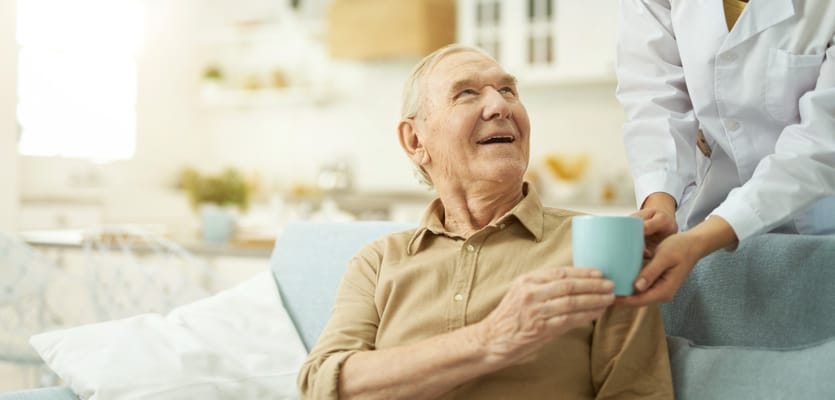 A caregiver serving a drink to a smiling elderly resident
