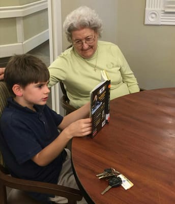 A young boy reading to an elderly woman at a table
