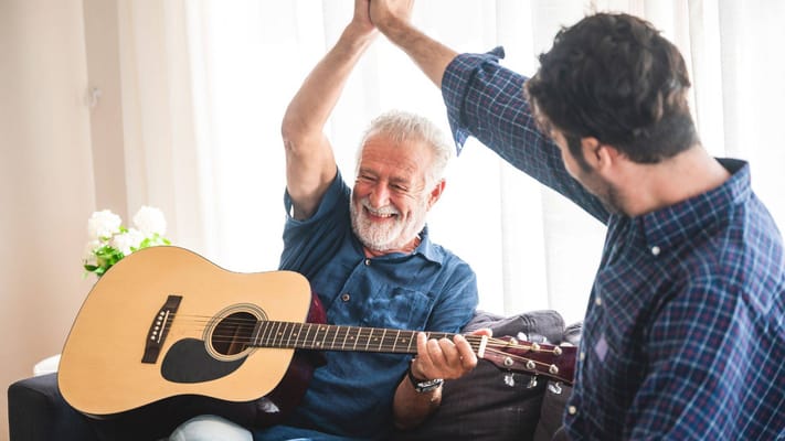 A resident playing guitar with staff in a joyful activity