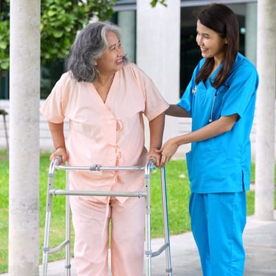 A senior resident with a walker assisted by a caregiver outdoors