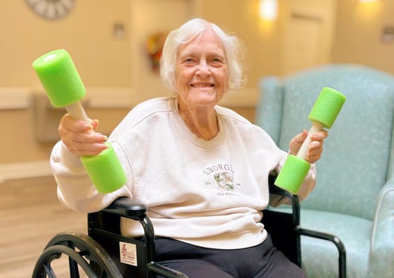 Resident exercising with green foam weights in a bright activity room