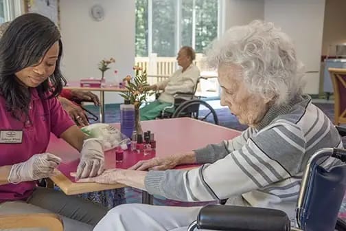Resident receiving a manicure from staff in an activity room