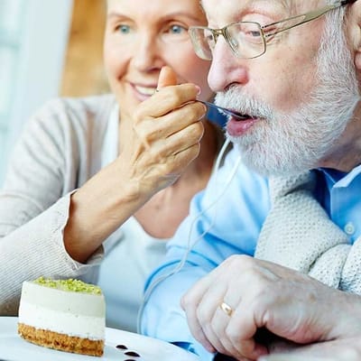 A senior man enjoying dessert with a caregiver.