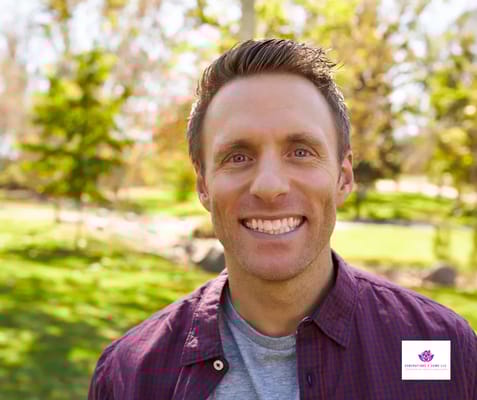 A smiling man in a park setting with greenery