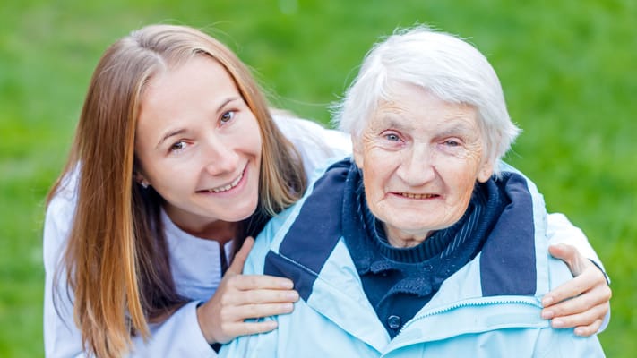 A caregiver smiling with an elderly resident outdoors