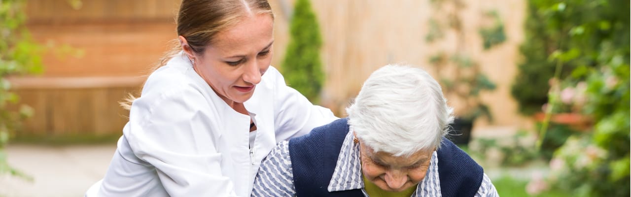 Staff assisting a senior resident in a garden area