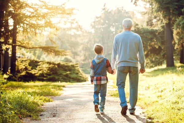 An elderly man holding hands with a child in a park