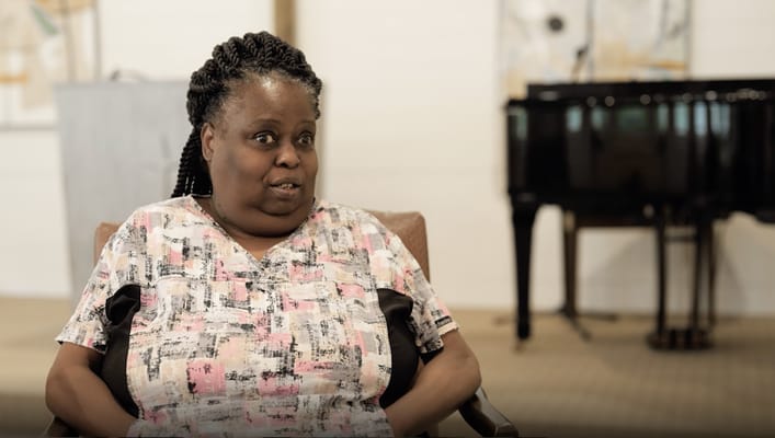 Resident in a facility setting, seated with a piano in the background