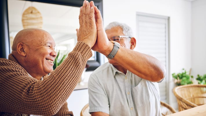Two elderly men high-fiving in a warm setting