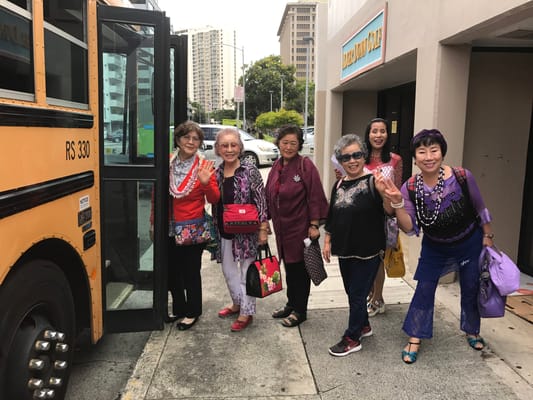 Residents boarding a bus with smiles and leis