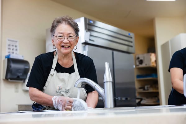 A resident smiling while washing dishes in the kitchen