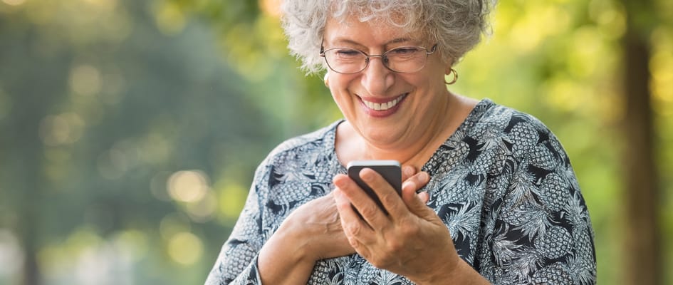Elderly woman smiling at her smartphone outdoors