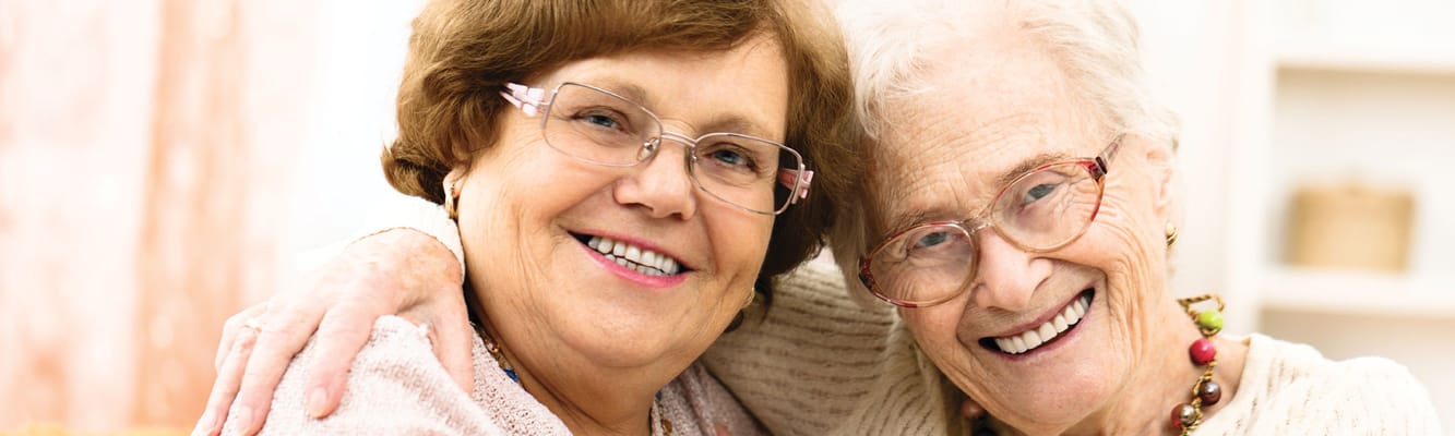 Two elderly women smiling and embracing