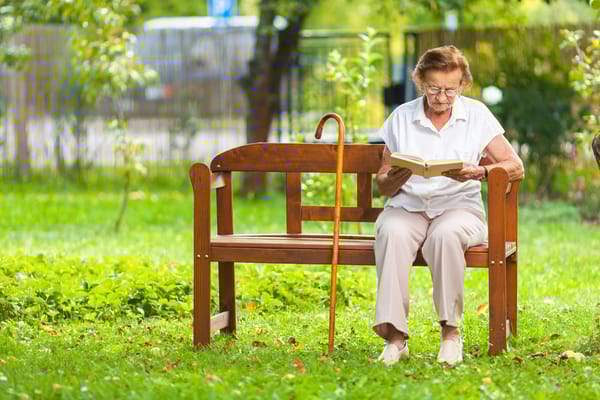 An elderly woman reading on a bench in a garden