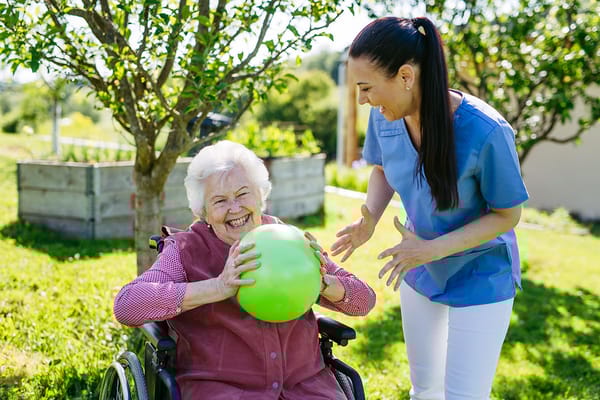 A caregiver and resident enjoying outdoor playtime with a ball.
