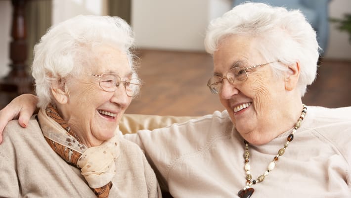 Two elderly women smiling together on a couch