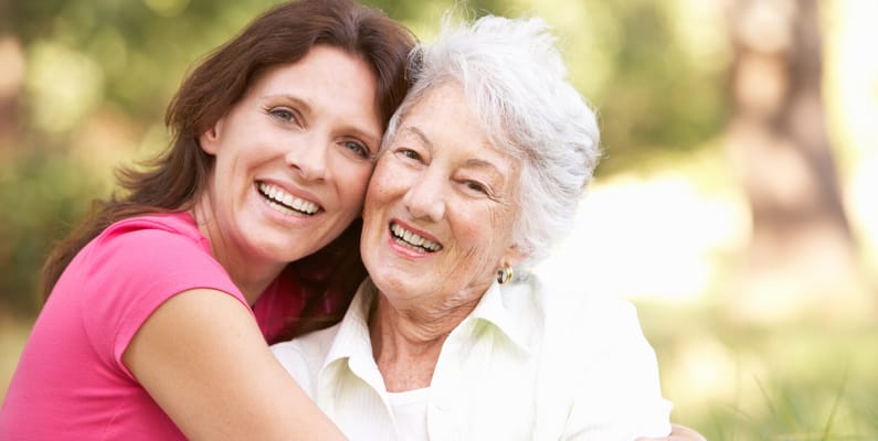A resident and staff member smiling together outdoors