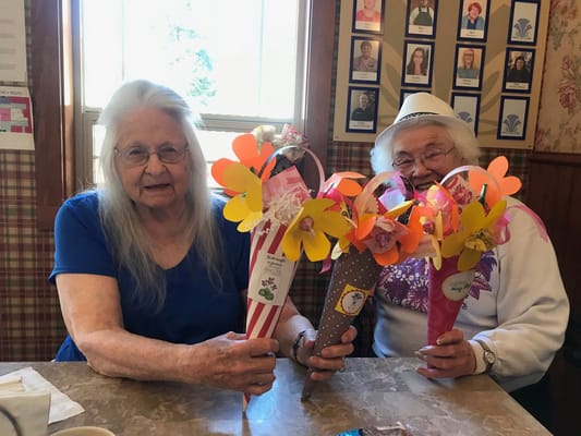 Two residents showcasing craft flowers indoors
