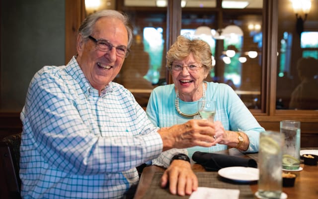 Two smiling residents toasting in a dining setting