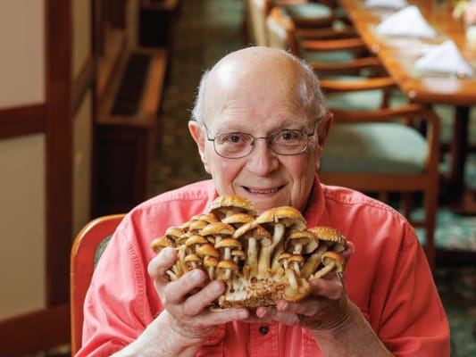 An elderly man holding a large mushroom in a dining setting