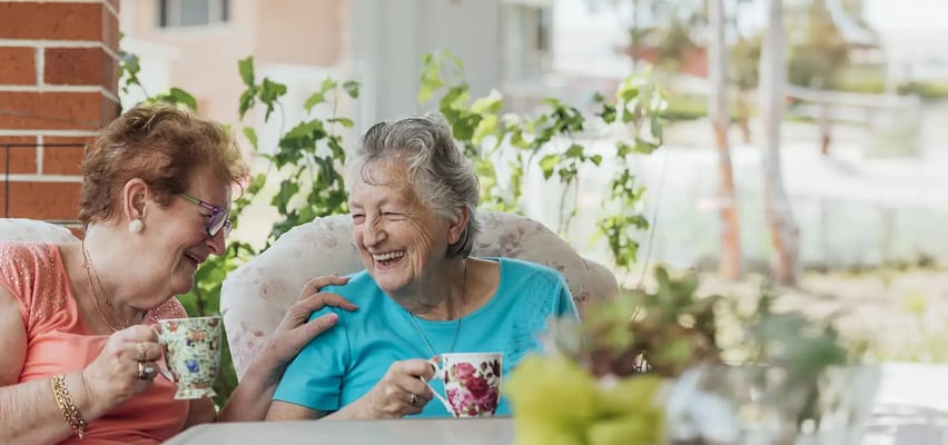 Two residents enjoying tea and laughter in a sunny garden